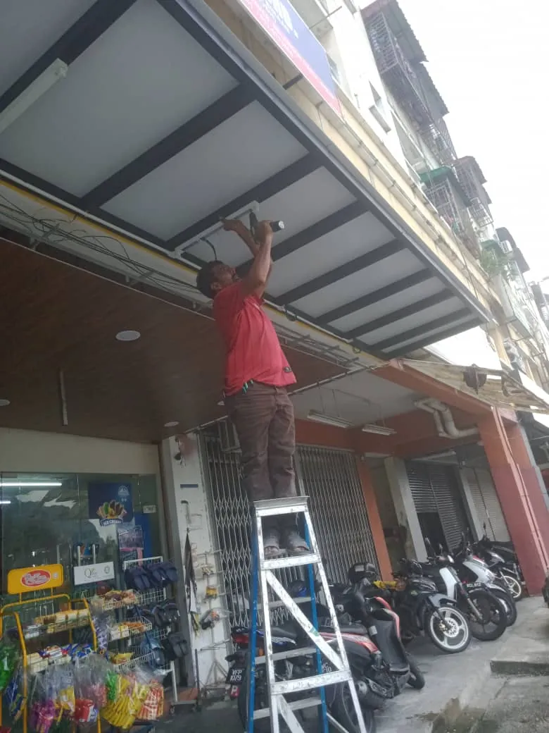 Renovix Home Services 工人在吉隆坡街边店屋雨棚天花上安装灯板。