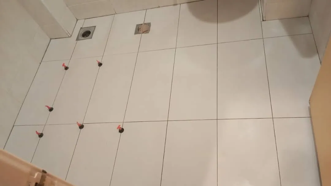Renovix Home Services 在吉隆坡围绕地漏铺贴带红色调平卡扣的大规格地砖。