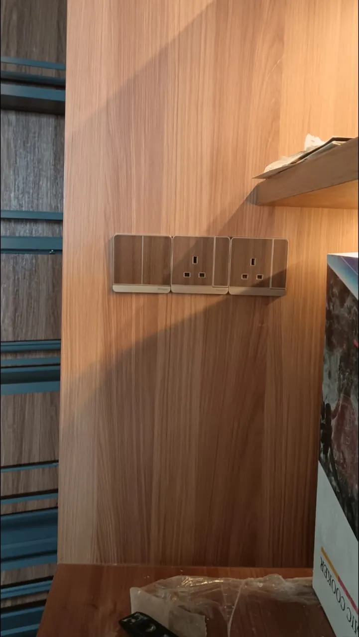 Three wood-grain switch and socket plates installed in a row on a timber wall panel by Renovix Home Services in Kuala Lumpur.